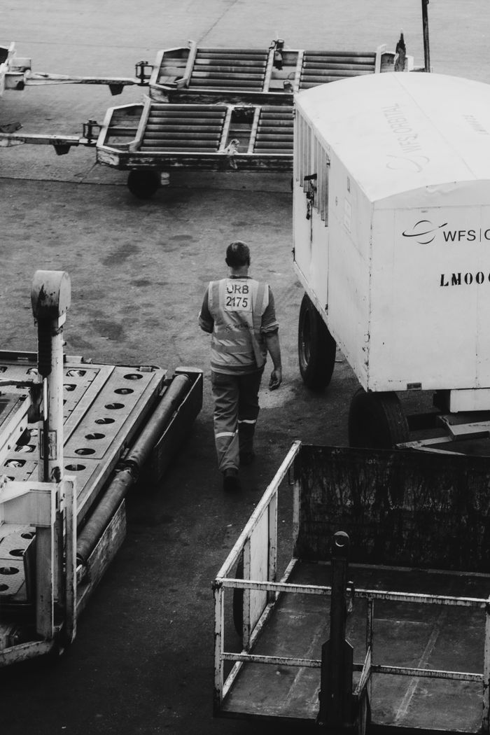 Worker in reflective vest among cargo equipment at an airport, monochrome shot.
